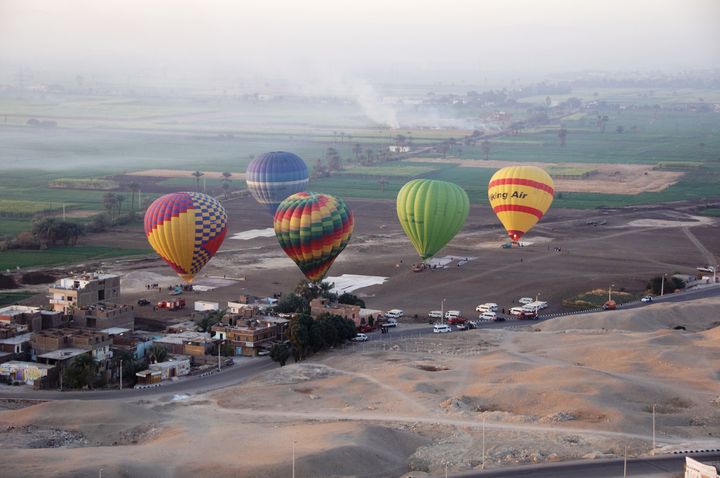 Bunte Heißluftballons schweben im Morgendunst über Feldern und Dörfern am Nil bei Luxor